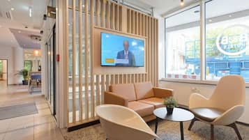 Eine moderne Hotelhalle mit Fernseher, Sitzgelegenheiten und großen Fenstern.