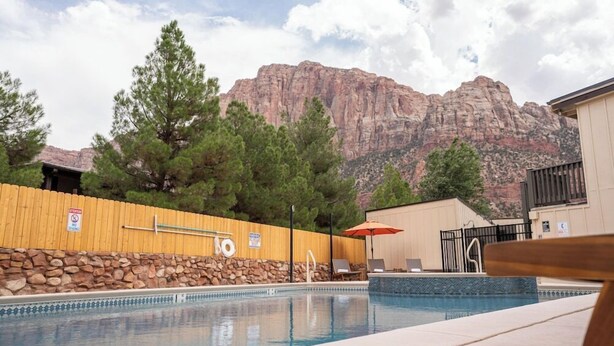 A pool with a wooden fence, lounge chairs, and a mountain backdrop. - Zion Pioneer Lodge (Springdale)