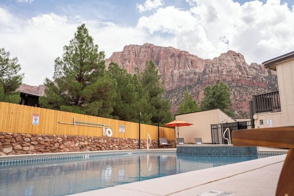 A pool with a wooden fence, lounge chairs, and a mountain backdrop. - Zion Pioneer Lodge (Springdale)