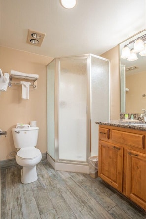 A bathroom with a toilet, shower, and wooden vanity with a mirror. - Zion Pioneer Lodge (Springdale)