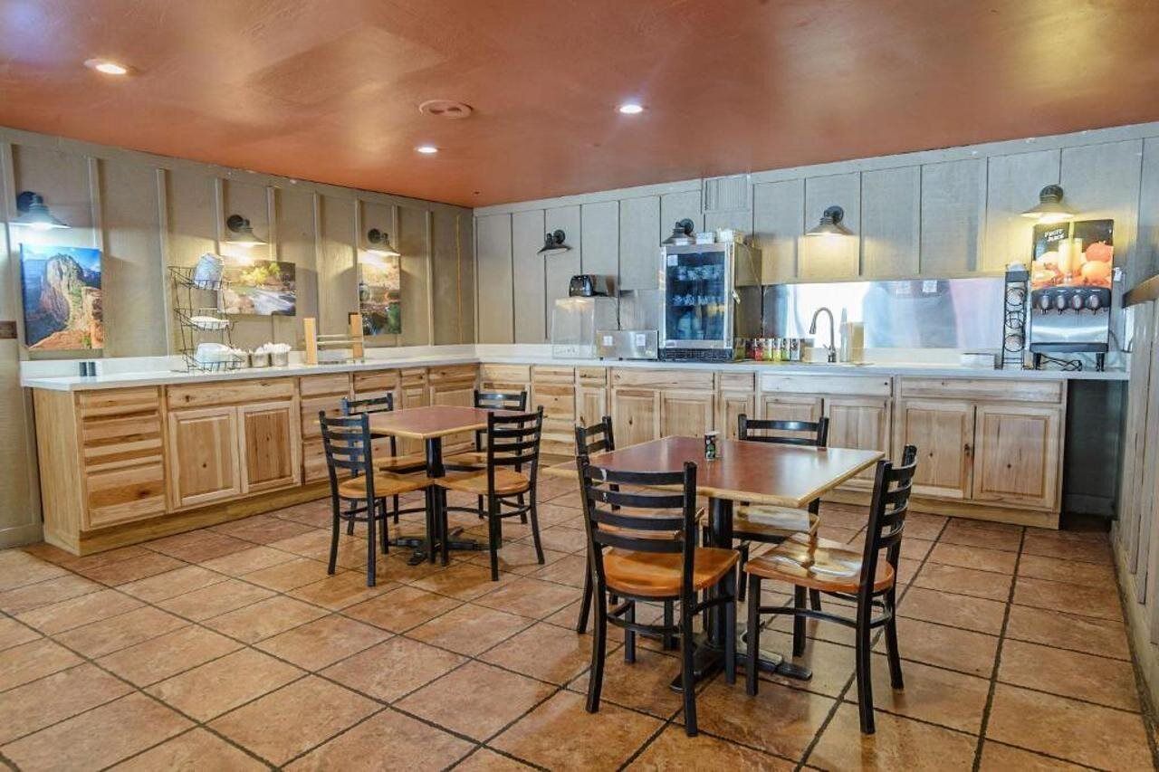 A kitchen with wooden cabinets, a central island with chairs, a refrigerator, and a coffee machine.