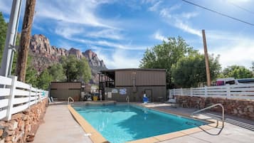 A pool area with a clear view of mountains in the background, a white fence, and a building with a sign.