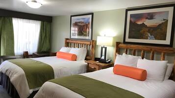A hotel room with two beds, green curtains, a desk, and a nightstand with a lamp.