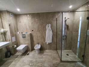 A bathroom with a glass-enclosed shower, a bidet, a toilet, and a robe hanging on the wall. - Hotel Moonlight Path (Nessebar)