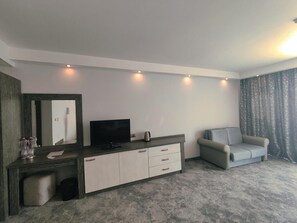 A modern hotel room with a flat-screen TV, a sofa, a small table, and a large window with curtains. - Hotel Moonlight Path (Nessebar)