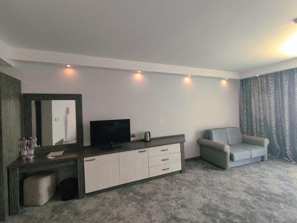A modern hotel room with a flat-screen TV, a sofa, a small table, and a large window with curtains. - Hotel Moonlight Path (Nessebar)