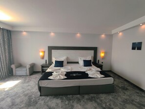 A hotel room with a large bed, two bedside tables, a chair, and wall-mounted lights. - Hotel Moonlight Path (Nessebar)