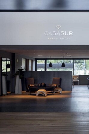 A modern hotel lobby with a reception desk, seating area, and large windows. - Casasur Pilar Hotel (La Lonja)