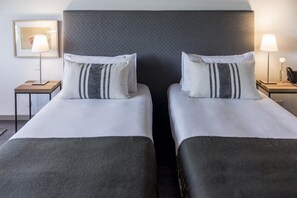 Quarto de hotel com duas camas, cada uma com travesseiro e mesa de cabeceira com abajur.