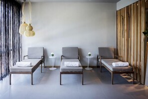 Een moderne spa-ruimte met drie grijze lounge fauteuils, kleine ronde tafels en een houten wandpaneel.