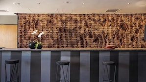 A bar area with a unique wooden wall, three stools, and a vase with flowers. - Casasur Pilar Hotel (La Lonja)