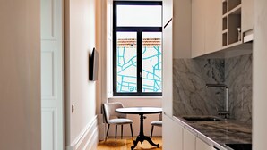 Un corridoio stretto con pavimento decorato, una sala da pranzo con tavolo e sedie, e una cucina con pensili e un piano di lavoro.