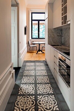 A narrow hallway with patterned flooring, a dining area with a table and chairs, and a kitchen with cabinets and a countertop. - Opulent Historic Palace Suite w/ Terrace Overlooking Porto’s Historic Center 1J (Porto)