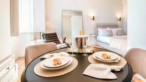 Camera d'albergo moderna con tavolo da pranzo apparecchiato per due, un letto con lenzuola bianche e un grande specchio.