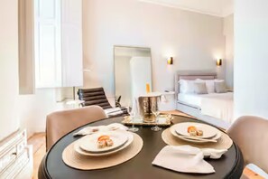 A modern hotel room with a dining table set for two, a bed with white linens, and a large mirror. - Opulent Historic Palace Suite w/ Terrace Overlooking Porto’s Historic Center 1J (Porto)