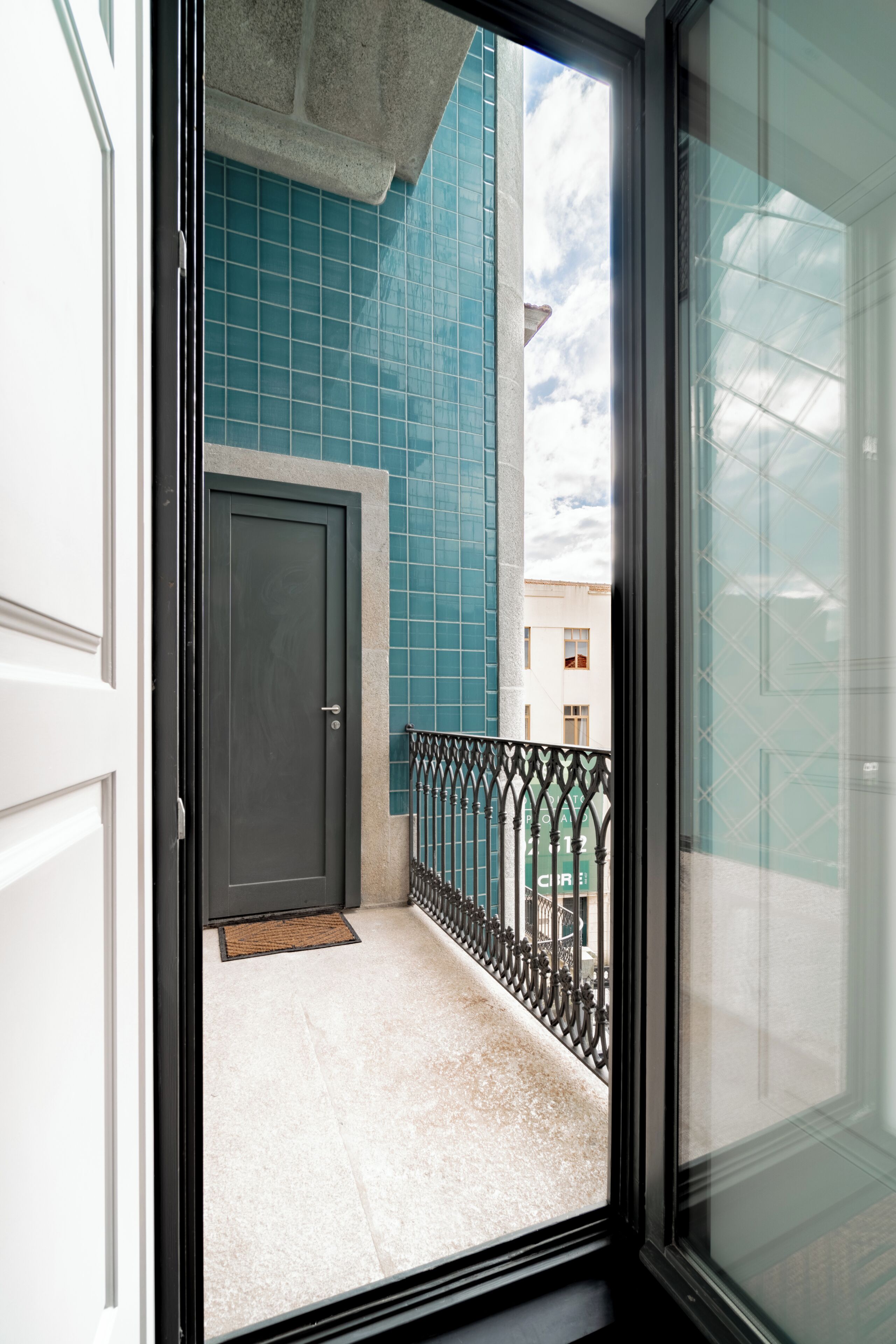 A view through a glass door to a balcony with a tiled wall, a door, and a metal railing.
