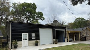 A two-story building with a garage, a covered porch, and a brick structure adjacent to it. - Cozy 1-bedroom cottage in serene Ravenel with AC (Ravenel)