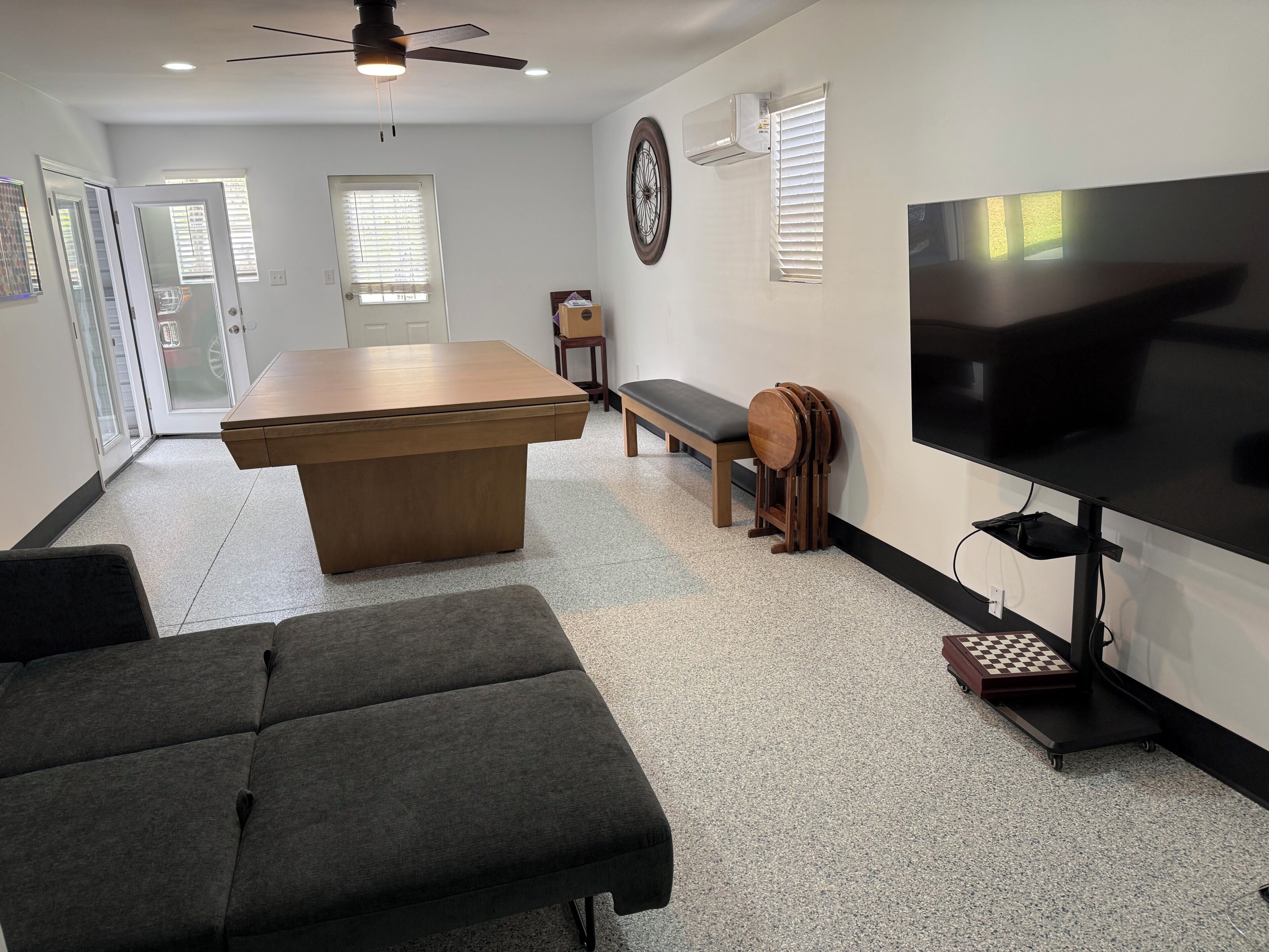 A modern living room with a wooden coffee table, a grey sofa, a TV, and a ceiling fan.