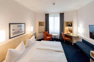 Habitación de hotel con dos camas, un escritorio, una silla, un televisor y un cuadro en la pared.