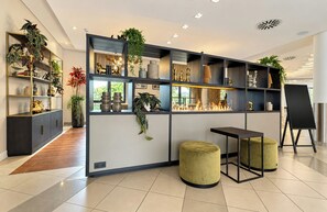 A modern interior with a sectional wall unit, two ottomans, a black table, and a blackboard. - Intercityhotel Magdeburg (Magdeburg)