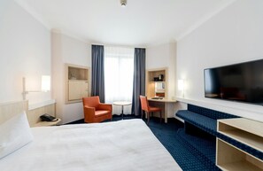 Ein Hotelzimmer mit einem großen Bett, einem Schreibtisch mit Stuhl, einem Fernseher und einem Sofa.