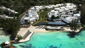 Vista aérea de un resort con varias construcciones blancas, un área de piscina central y una playa.