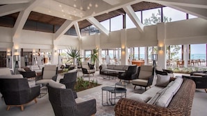 Un espacio interior amplio con muebles de mimbre, ventanas grandes y vista al mar.