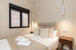 Ein Schlafzimmer mit Bett, Kissen, einem Nachttisch, einem Fenster mit Jalousien und einer Wandleuchte.