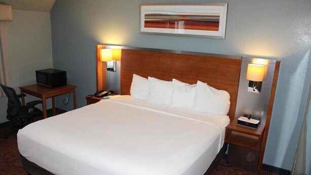 A hotel room with a large bed, two bedside tables with lamps, a desk with a computer, and a painting on the wall. - Clarion Hotel Bakersfield North (Bakersfield)