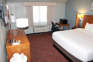 Una camera d'albergo con un letto, una scrivania con lampada, una sedia, televisore, telefono e una finestra con tende.