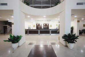 A reception area with a reception desk, two potted plants, and a staircase in the background. - Sun Palace Hotel - All Inclusive (Nessebar)
