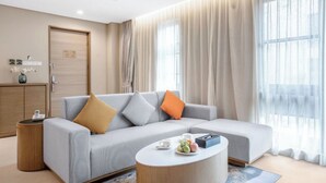 A modern hotel room with a grey sofa, a round coffee table, and a bed. - CM+ Serviced Apartment Shenzhen Hillside (Shenzhen)