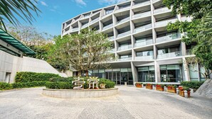 A modern building with a curved facade, a landscaped courtyard with a central tree, and a sign with Chinese characters. - CM+ Serviced Apartment Shenzhen Hillside (Shenzhen)