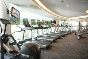 Een fitnessruimte met loopbanden, fitnessballen en een televisiescherm.