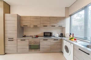 A modern kitchen with built-in appliances, a washing machine, and a window with blinds. - CM+ Serviced Apartment Shenzhen Hillside (Shenzhen)