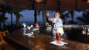 A bar area with a wooden table, a drink, and a view of the ocean. - Diani Reef Beach Resort and Spa (Diani Beach)