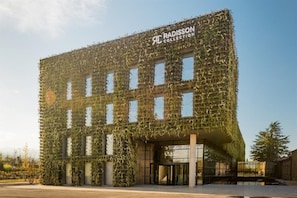Un edificio con fachada cubierta de hiedra, una entrada de vidrio y el logotipo de Radisson Collection.