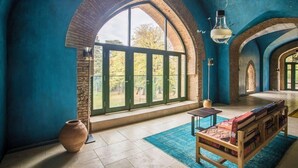 A room with a large arched window, a wooden bench, a table, and a vase.