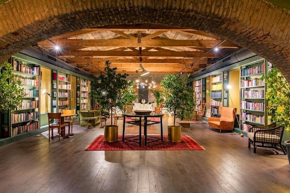 Une bibliothÚque intérieure avec des étagÚres, une table centrale, des chaises et des plantes en pot.