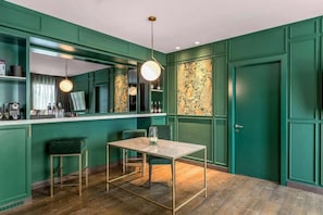 Una habitación con pared verde, suelo de madera, una mesa con sillas y una lámpara colgante.