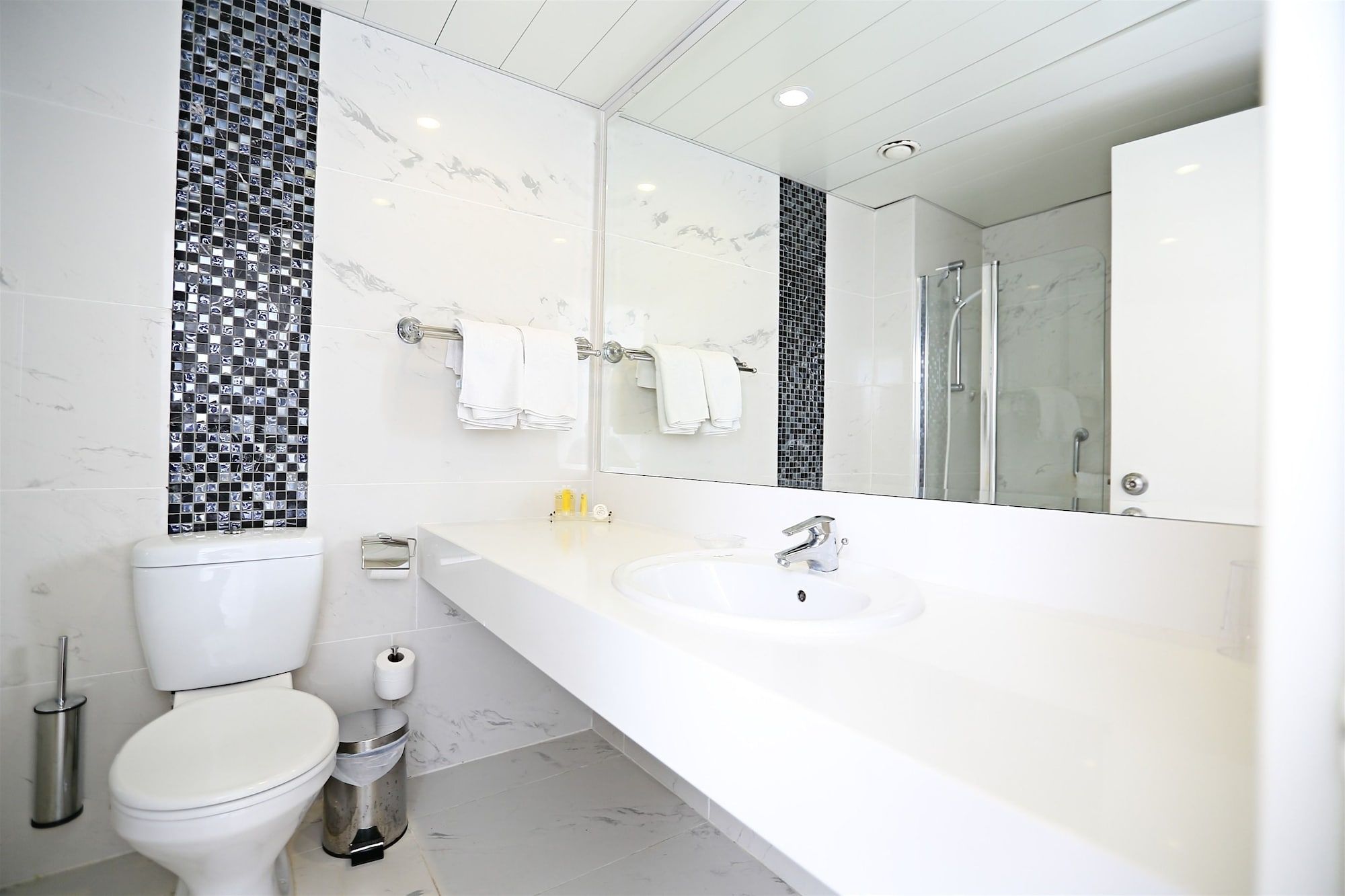 A modern bathroom with a toilet, bidet, and a large mirror above a white sink.
