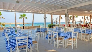 An outdoor dining area with checkered tablecloths, white chairs, and a view of the sea. - Dome Beach Marina Hotel and Resort (Ayia Napa)