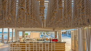 A beachside bar with a wooden deck, white bar stools, and a view of the ocean. - Dome Beach Marina Hotel and Resort (Ayia Napa)