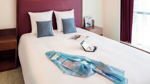A neatly made bed with a red headboard, two pillows, a smartphone, and a folded blue scarf on the bed. - Adagio Fujairah (Al-Fujairah)