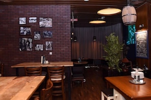 Interior de restaurante com paredes de tijolo, mesas e cadeiras de madeira, luminárias pendentes e um quadro de cardápio.