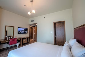 Quarto de hotel com cama, televisão, escrivaninha e porta.