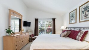 Un dormitorio con una cama grande, un aparador de madera, un televisor y una ventana con cortinas.