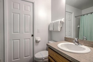 Un baño con inodoro blanco, lavabo con espejo arriba y cortina de ducha.