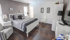 Un dormitorio con una cama, una silla, un televisor y un ventilador de techo.