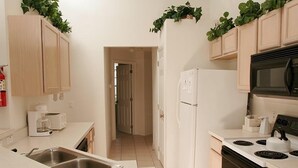 Una cocina compacta con encimera blanca, estufa, microondas y refrigerador.